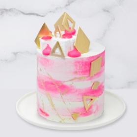 The “Geometric, Gold & Cerise Watercolour” Cake is a buttercream iced cake. The single tier is 6″ deep and 2 tier options are 10″ deep. This cake also includes chocolate gems, marshmallows and the geometrics shapes are also edible. A name plaque can be added to the front of the cake.